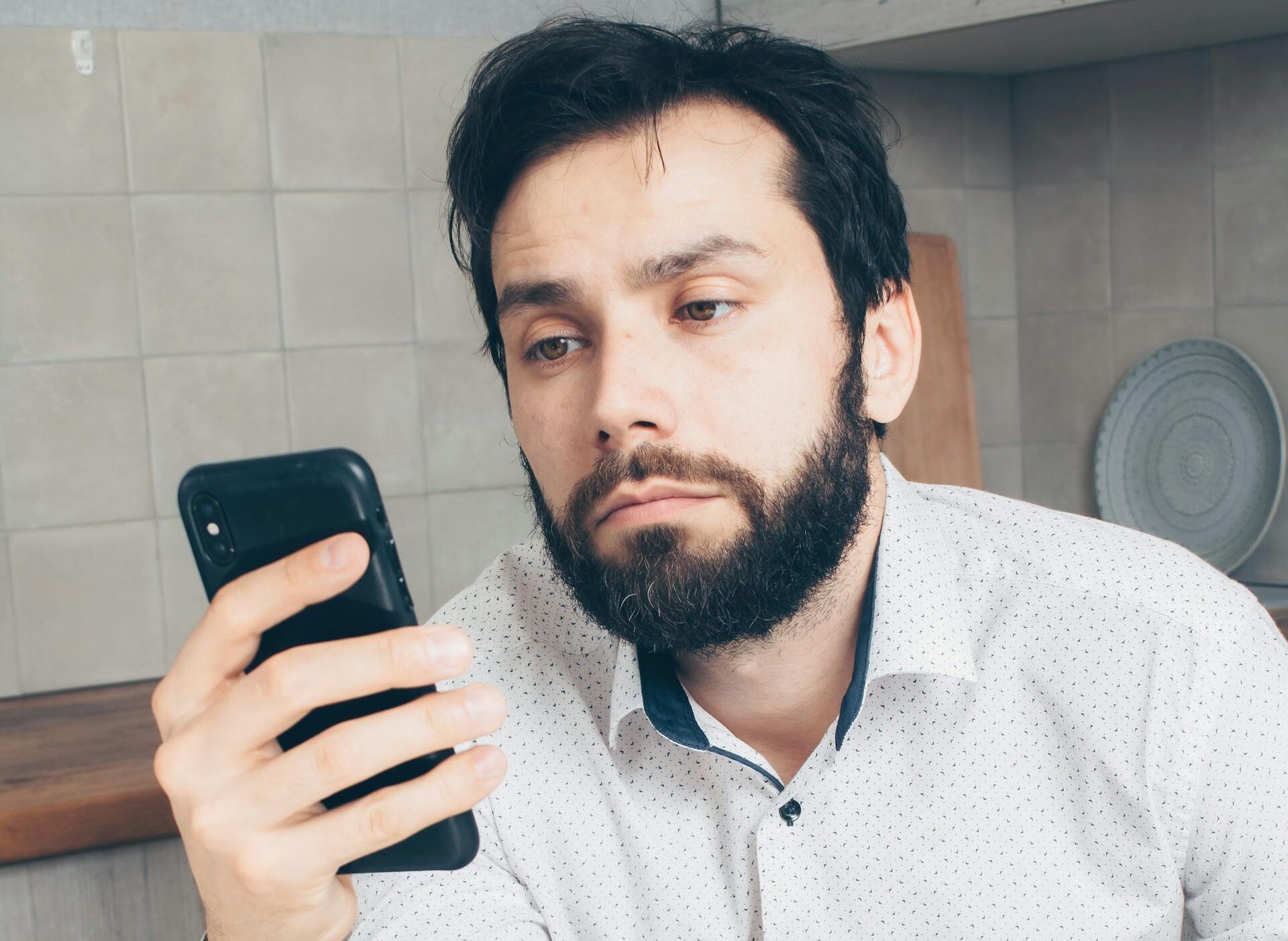 A man looks frustrated while checking his smartphone, possibly experiencing a banking issue or scam.